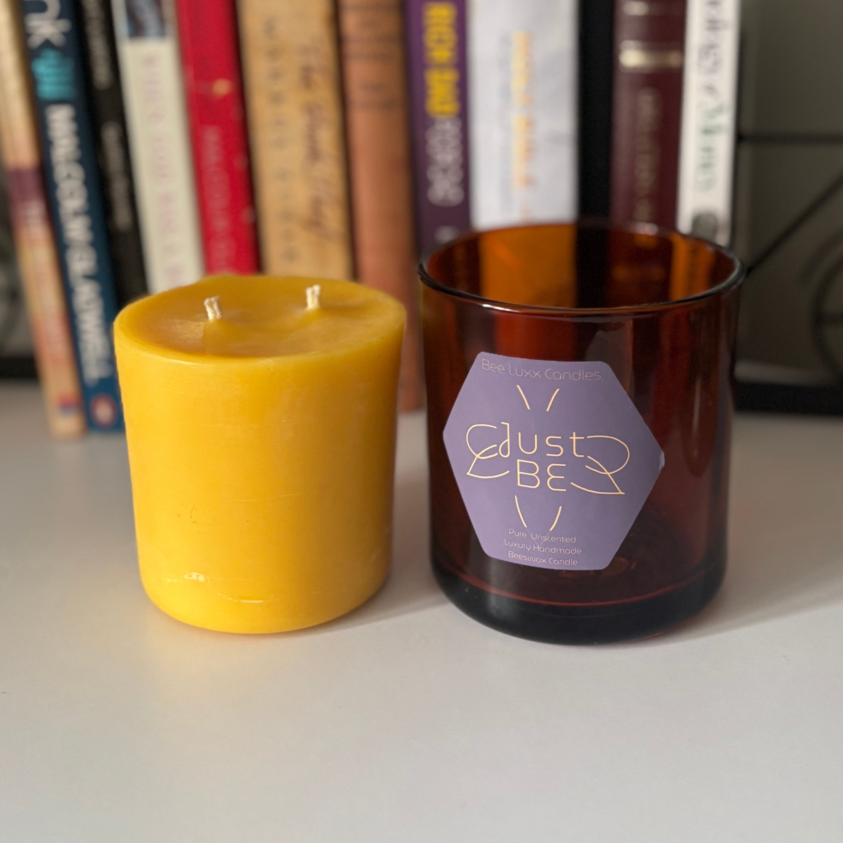 Candle refill and one empty brown candle jar with a label, on a surface with books and a plant in the background.