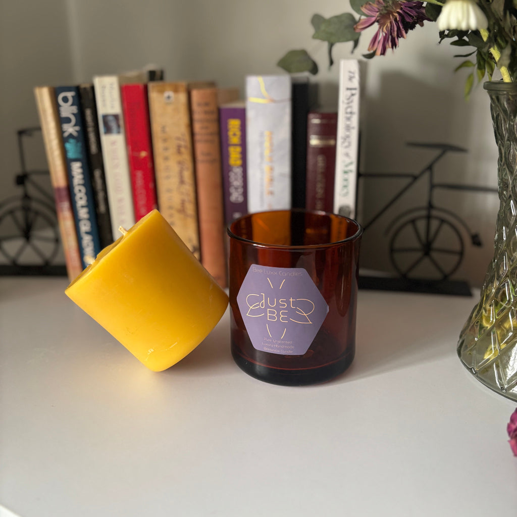 Empty candle jar with a yellow candle refill and books on a surface